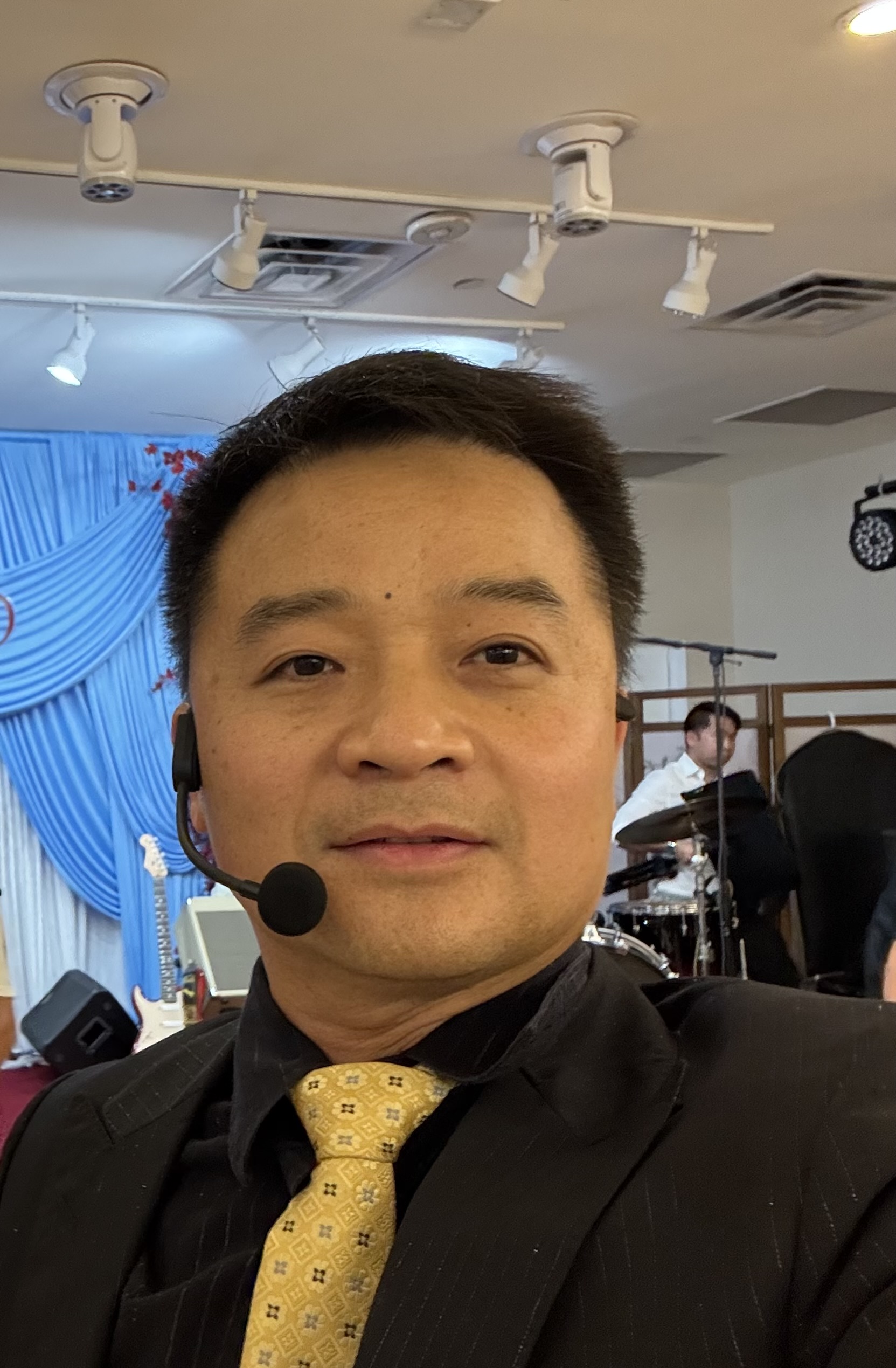 DJ MC Thinh wearing a suit and headset microphone at an event